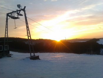 Die Sonne geht unter über dem Sauerland. Durch die Flutlichtbeleuchtung ist Skifahren am Grevenstein Skilift jedoch auch abends möglich.